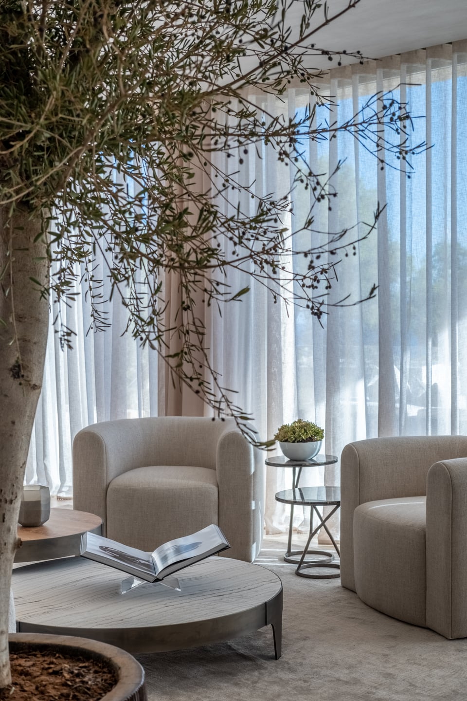 Sculptural armchair positioned against soft full-height curtains